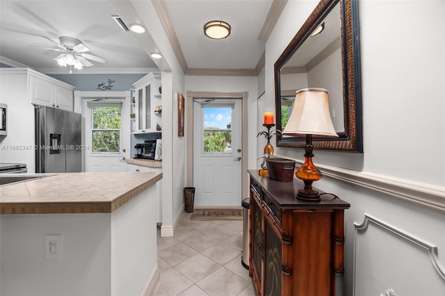 interior space with kitchen peninsula, ornamental molding, stainless steel fridge with ice dispenser, white cabinetry, and ceiling fan