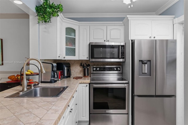 kitchen featuring appliances with stainless steel finishes, sink, white cabinetry, tile counters, and ornamental molding