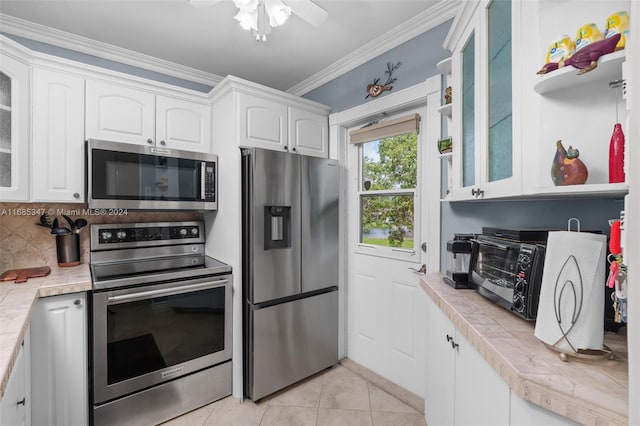 kitchen featuring appliances with stainless steel finishes, tile countertops, white cabinetry, crown molding, and decorative backsplash