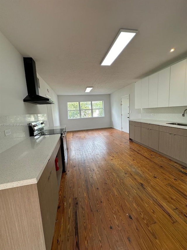 kitchen featuring wall chimney range hood, sink, stainless steel range with electric cooktop, white cabinets, and light hardwood / wood-style flooring