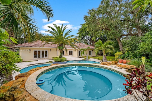 pool with french doors, a patio, and an in ground hot tub