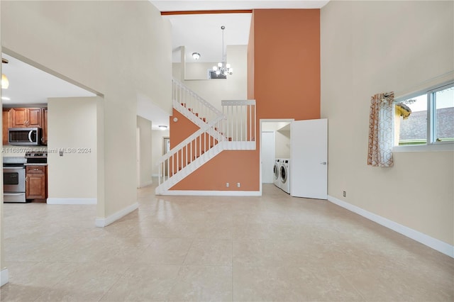 unfurnished living room featuring a towering ceiling, washing machine and dryer, light tile patterned floors, and a chandelier