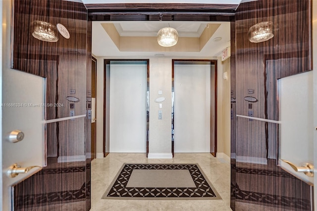 foyer with crown molding, a raised ceiling, and elevator