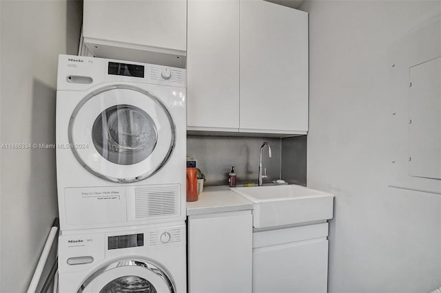 clothes washing area featuring sink, stacked washer / dryer, and cabinets