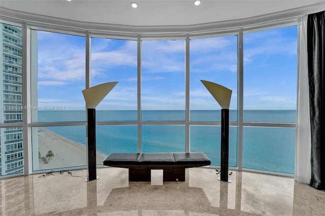 unfurnished sunroom with a water view, a view of the beach, and a healthy amount of sunlight