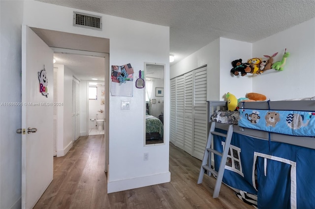 hallway with visible vents, a textured ceiling, and wood finished floors