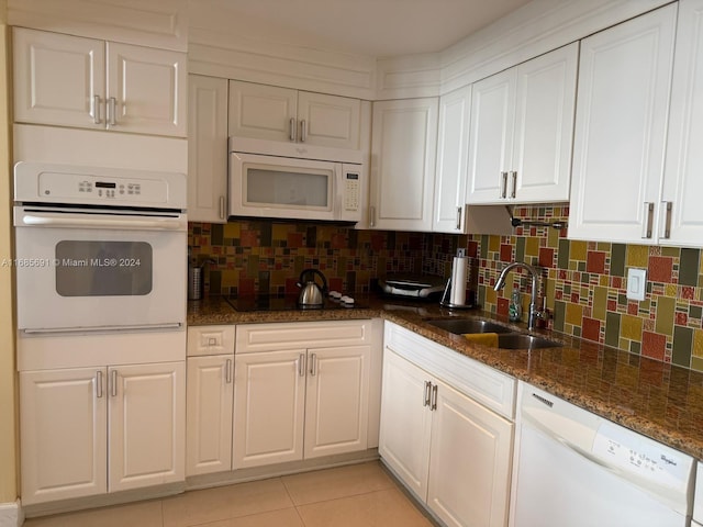 kitchen with dark stone counters, sink, light tile patterned floors, white cabinetry, and white appliances