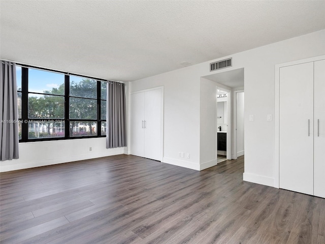 unfurnished bedroom featuring ensuite bath, dark wood-type flooring, and a textured ceiling