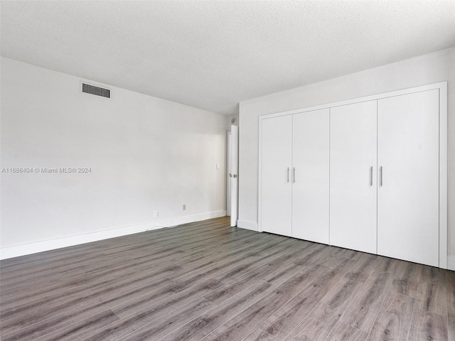 unfurnished bedroom featuring dark wood-type flooring, a textured ceiling, and a closet