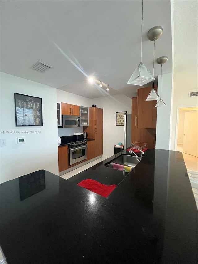 kitchen featuring a sink, hanging light fixtures, appliances with stainless steel finishes, brown cabinetry, and dark countertops