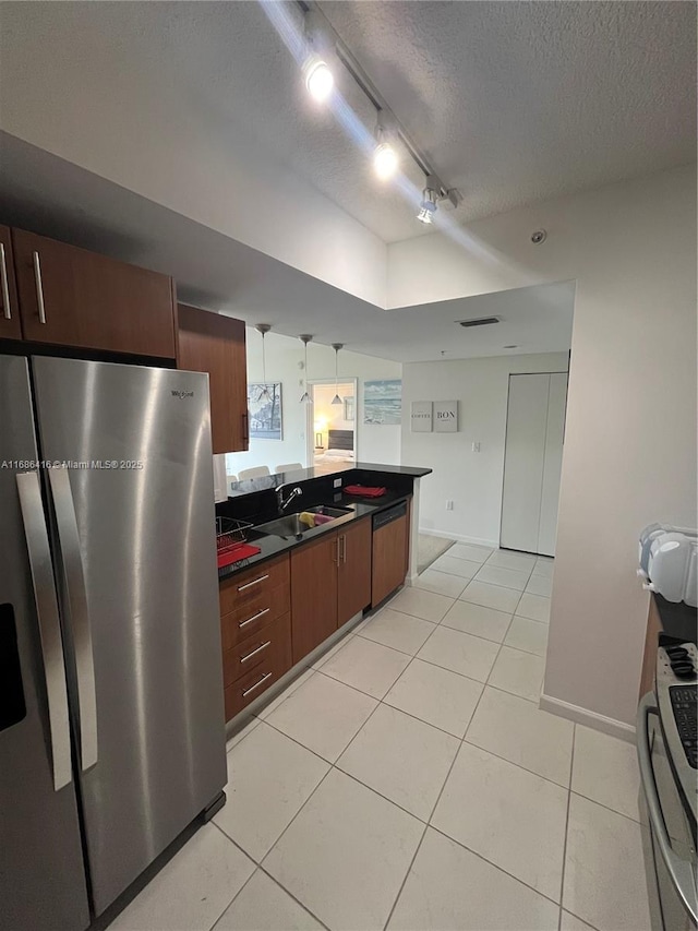 kitchen with decorative light fixtures, stainless steel appliances, dark countertops, a sink, and a textured ceiling