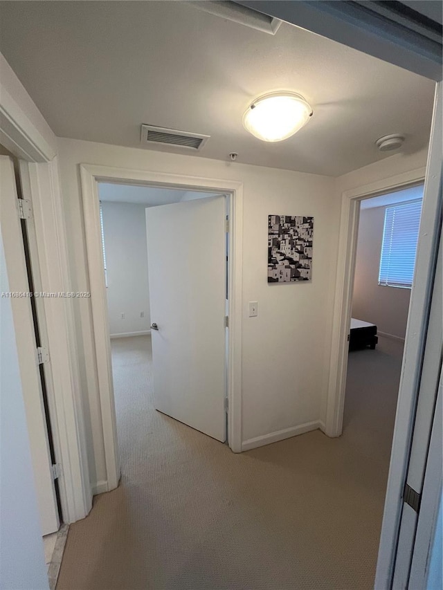 hall featuring light carpet, baseboards, and visible vents