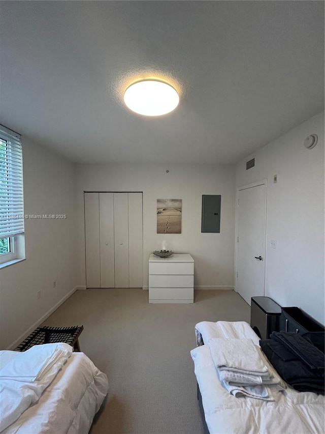 bedroom with light carpet, visible vents, baseboards, a closet, and electric panel