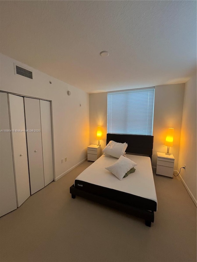 bedroom featuring a closet, visible vents, light carpet, a textured ceiling, and baseboards