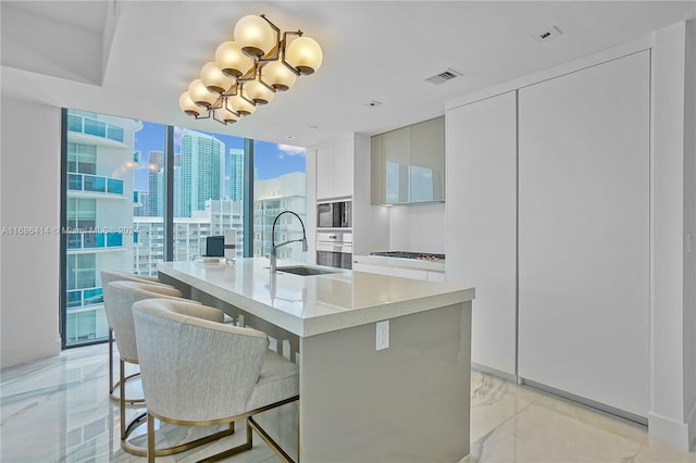 kitchen featuring expansive windows, a kitchen island with sink, a breakfast bar, white cabinets, and appliances with stainless steel finishes