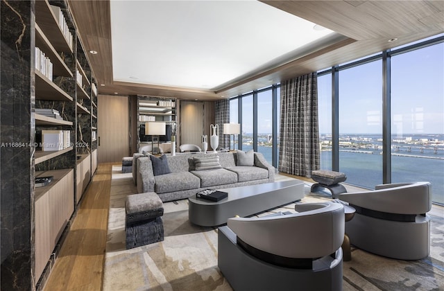 living room with a tray ceiling, a water view, wood-type flooring, and a wall of windows