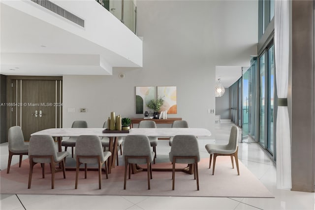 dining area with a towering ceiling, a notable chandelier, floor to ceiling windows, and light tile patterned floors