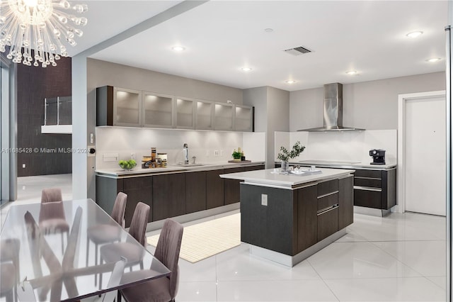 kitchen with cooktop, wall chimney range hood, sink, light tile patterned flooring, and a center island with sink