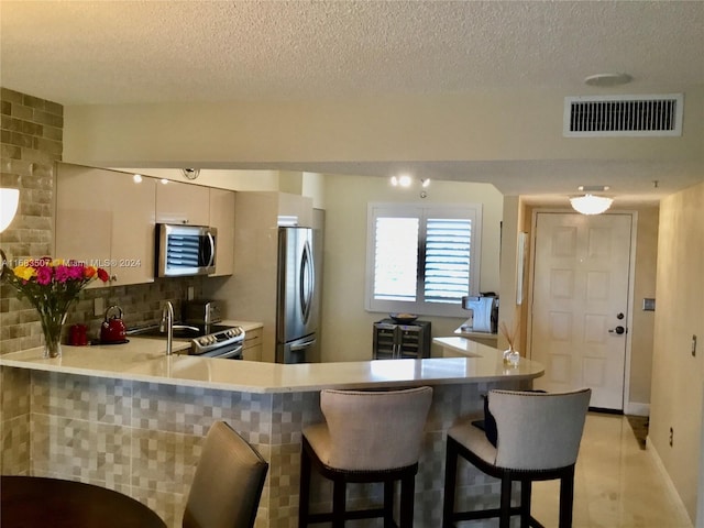 kitchen with appliances with stainless steel finishes, kitchen peninsula, a textured ceiling, and tasteful backsplash