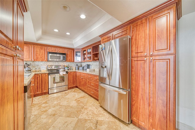 kitchen featuring backsplash, stainless steel appliances, light stone countertops, and a tray ceiling