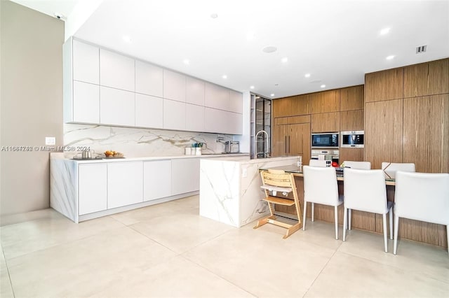 kitchen with a large island with sink, backsplash, a kitchen breakfast bar, white cabinets, and black microwave