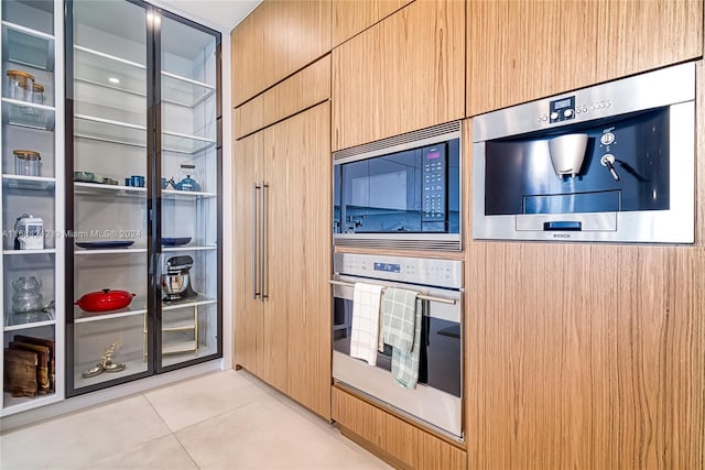 kitchen featuring built in microwave, stainless steel oven, and light tile patterned flooring