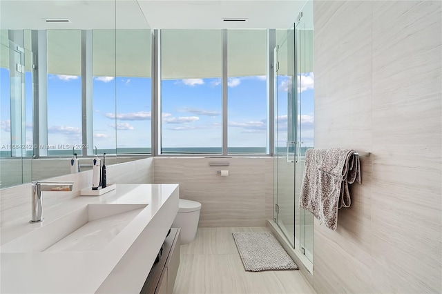 bathroom with tile walls, toilet, a shower with shower door, vanity, and a water view