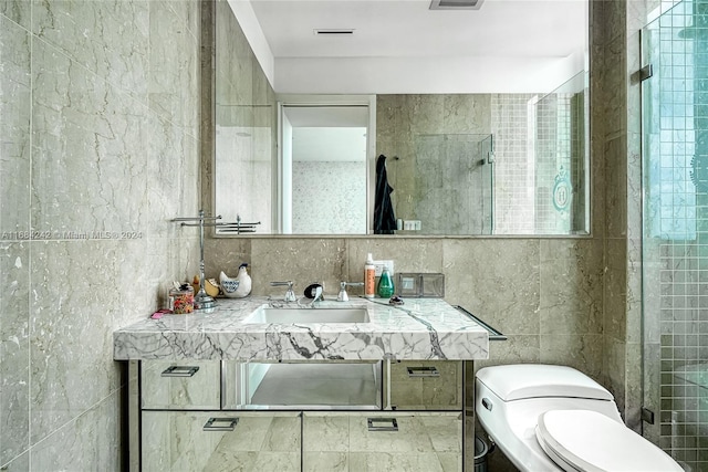 bathroom with toilet, a shower with shower door, vanity, and tile walls