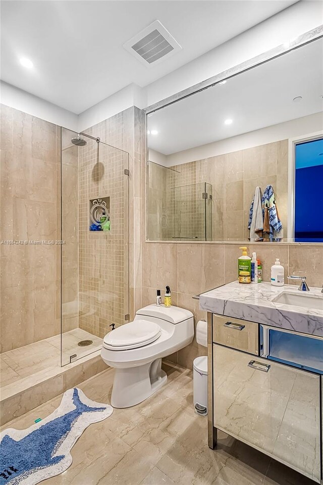 bathroom featuring tile walls, vanity, a tile shower, and toilet