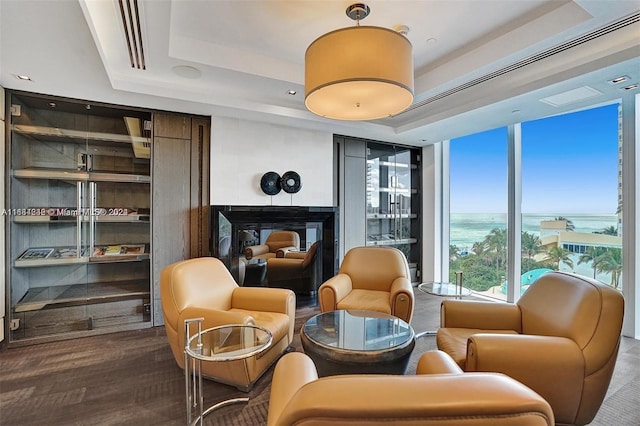 sitting room with a fireplace, a tray ceiling, wood-type flooring, a wall of windows, and a water view