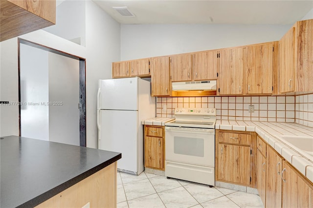 kitchen featuring visible vents, under cabinet range hood, vaulted ceiling, decorative backsplash, and white appliances