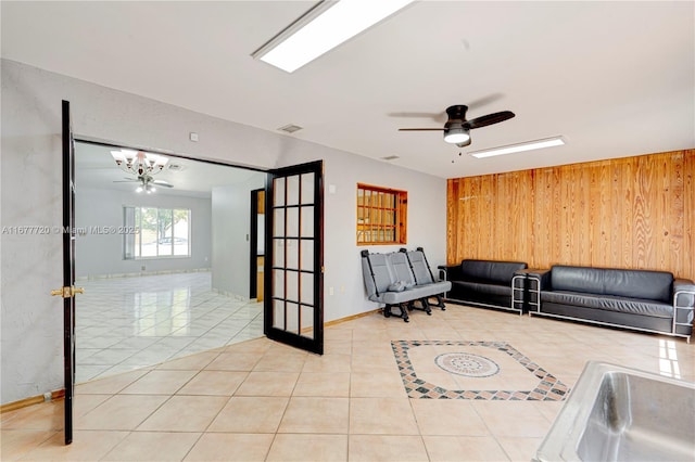 tiled living area with visible vents, baseboards, wood walls, and ceiling fan with notable chandelier