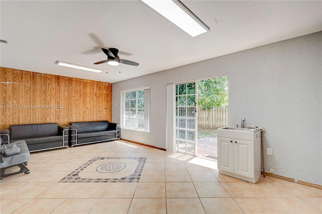 unfurnished living room featuring tile patterned floors, baseboards, wood walls, and a ceiling fan