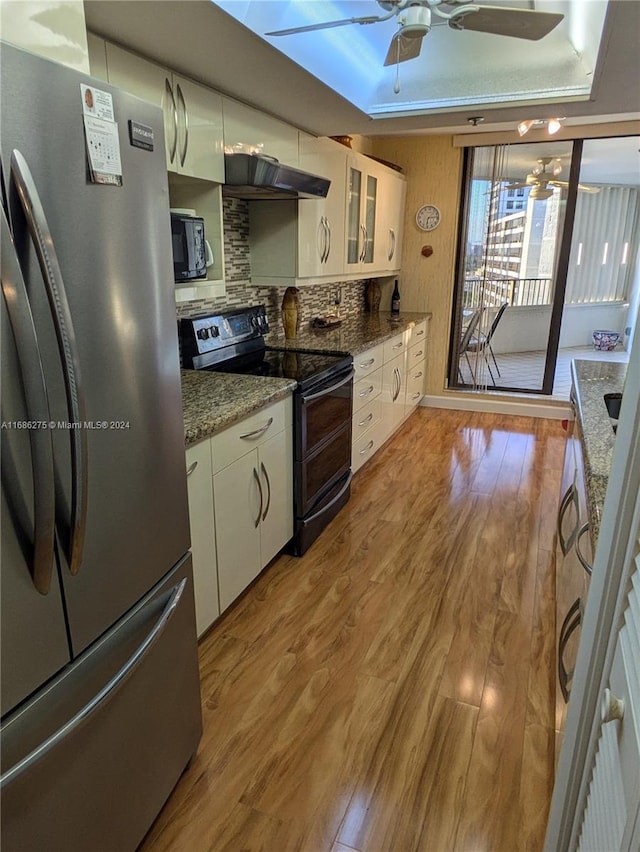 kitchen with tasteful backsplash, light hardwood / wood-style floors, a tray ceiling, white cabinets, and black appliances