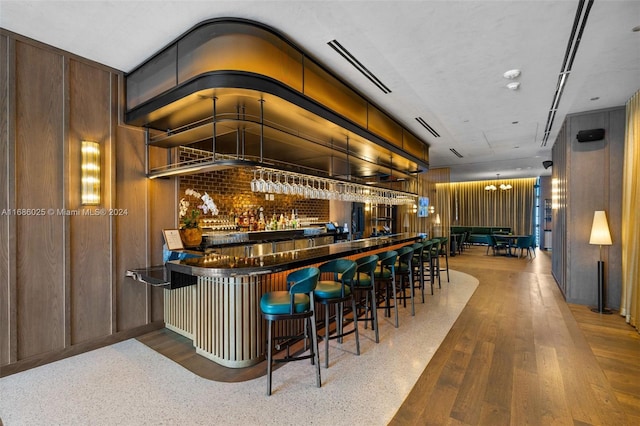 bar with hanging light fixtures, hardwood / wood-style floors, vaulted ceiling, wooden walls, and an inviting chandelier