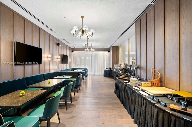 interior space with wooden walls, a textured ceiling, an inviting chandelier, and light wood-type flooring