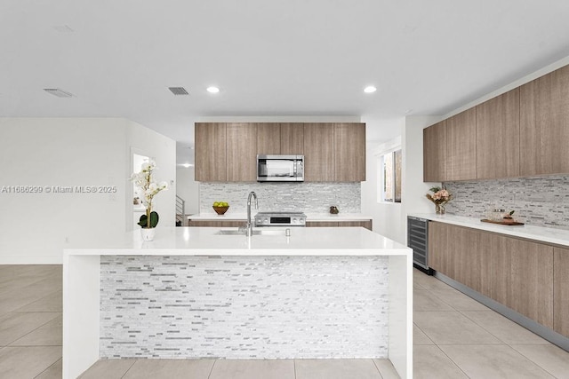 kitchen with light tile patterned flooring, sink, backsplash, and an island with sink