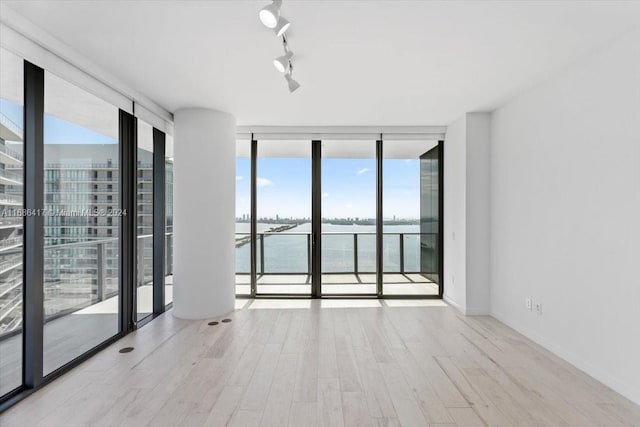 empty room featuring expansive windows, rail lighting, a water view, and light wood-type flooring