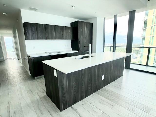 kitchen with sink, an island with sink, dark brown cabinetry, and light wood-type flooring