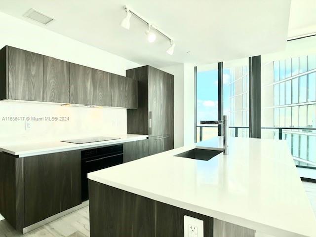 kitchen featuring black appliances, light hardwood / wood-style flooring, a center island with sink, and track lighting