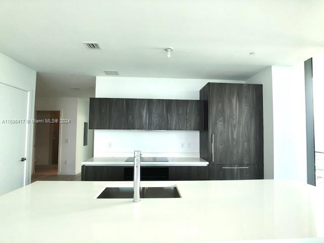 kitchen featuring stainless steel cooktop, dark brown cabinetry, and sink