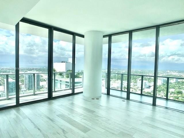 unfurnished room with wood-type flooring, plenty of natural light, and a wall of windows