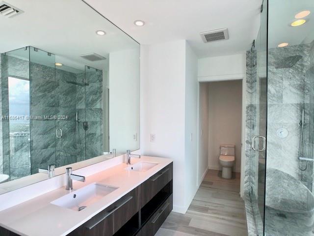 bathroom with vanity, toilet, a shower with shower door, and hardwood / wood-style floors