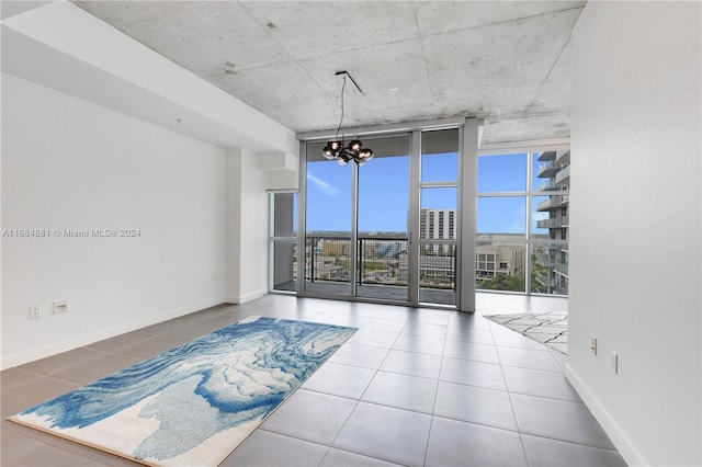 empty room with a notable chandelier, a healthy amount of sunlight, tile patterned flooring, and a wall of windows