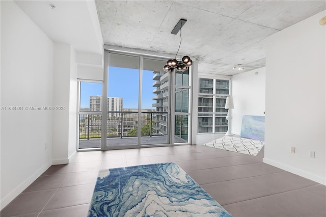 tiled empty room featuring expansive windows and a notable chandelier