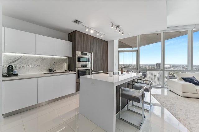 kitchen with white cabinets, backsplash, sink, dark brown cabinetry, and a center island