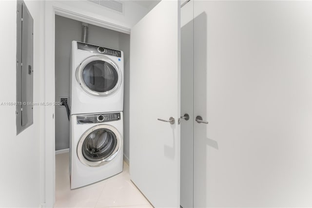 laundry area featuring electric panel, light tile patterned floors, and stacked washing maching and dryer