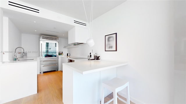 kitchen featuring kitchen peninsula, a breakfast bar, sink, light hardwood / wood-style flooring, and white cabinets