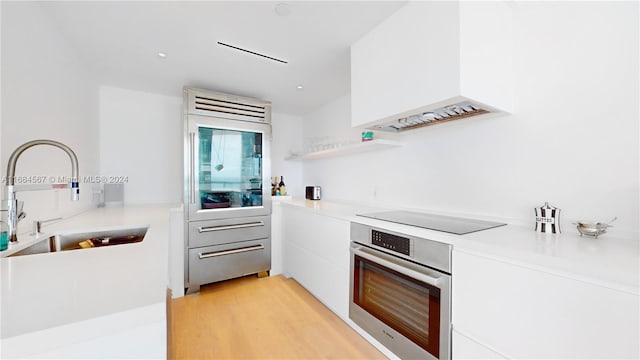 kitchen featuring light wood-type flooring, premium range hood, black electric cooktop, sink, and oven