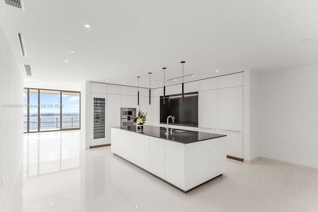 kitchen with dark countertops, pendant lighting, a center island with sink, and modern cabinets